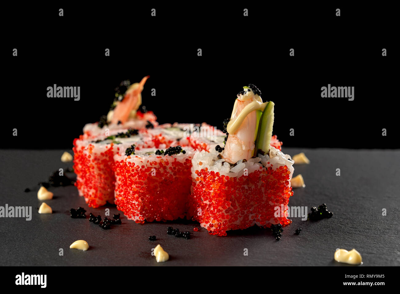 Japanese uramaki rice rolls with shrimps, cucumber, covered with red flying fish roe. Volcano sushi decorated with sauce and black caviar. Stock Photo