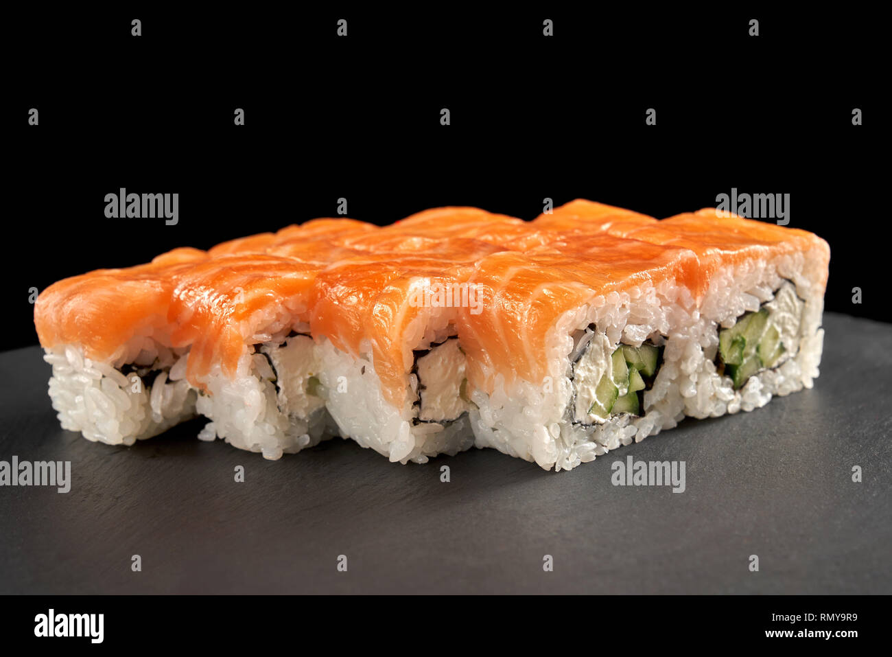 Uramaki philadelphia roll covered with salmon, filled with cucumber and  cream cheese. Philly rolls served on black stone slate plate Stock Photo -  Alamy