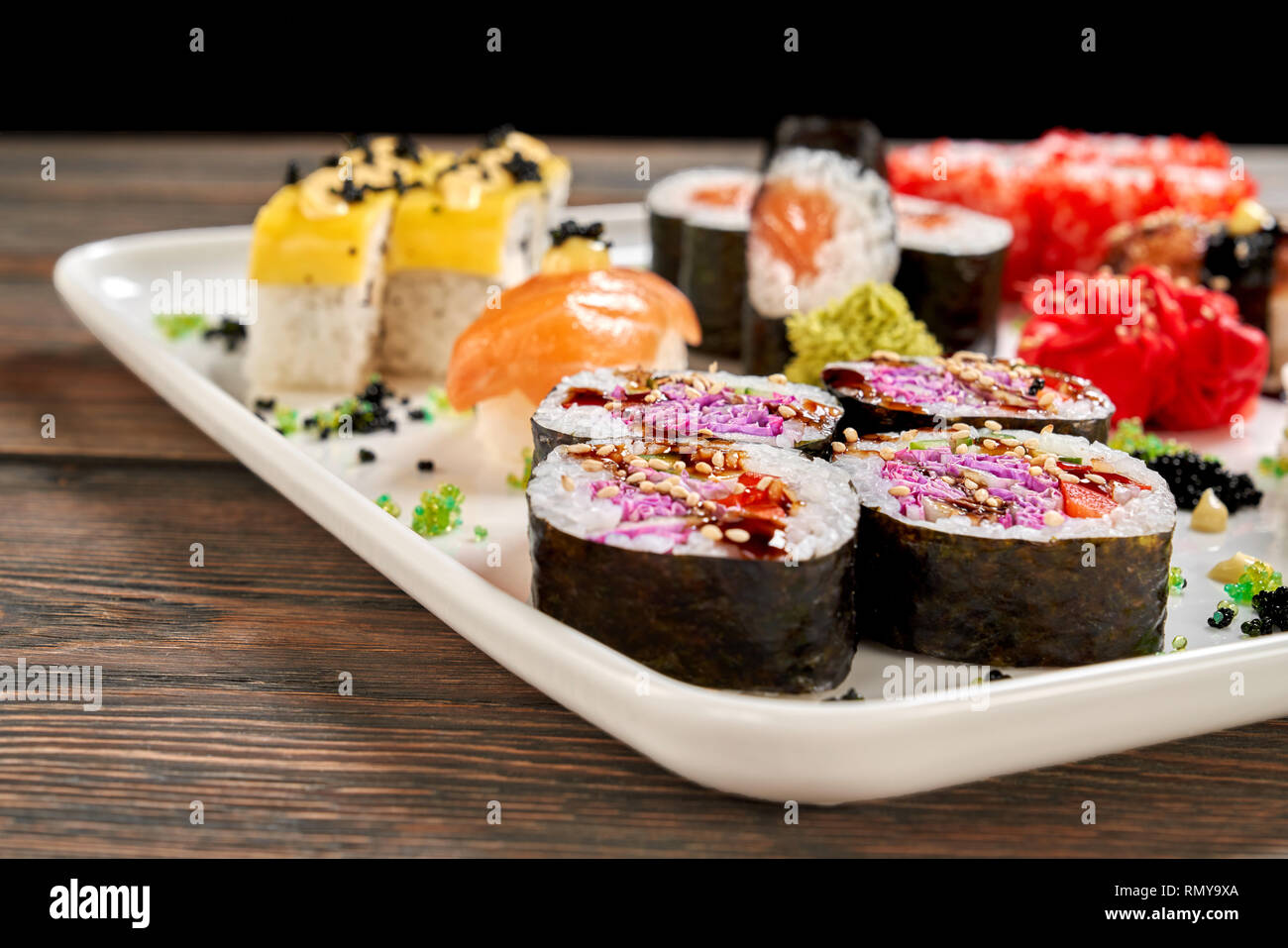 Vegetarian rolls close up, set of japanese sushi. Cheese rolls, sake nigiri and sake maki decorated with sauce, pickled ginger and wasabi, on white plate. Stock Photo