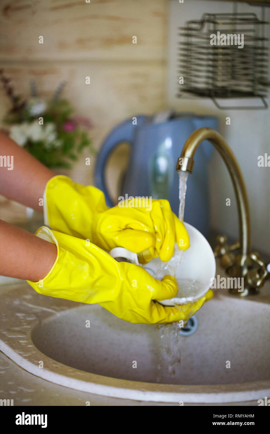 Close up hands of woman wearing yellow gloves washing dishes in kitchen