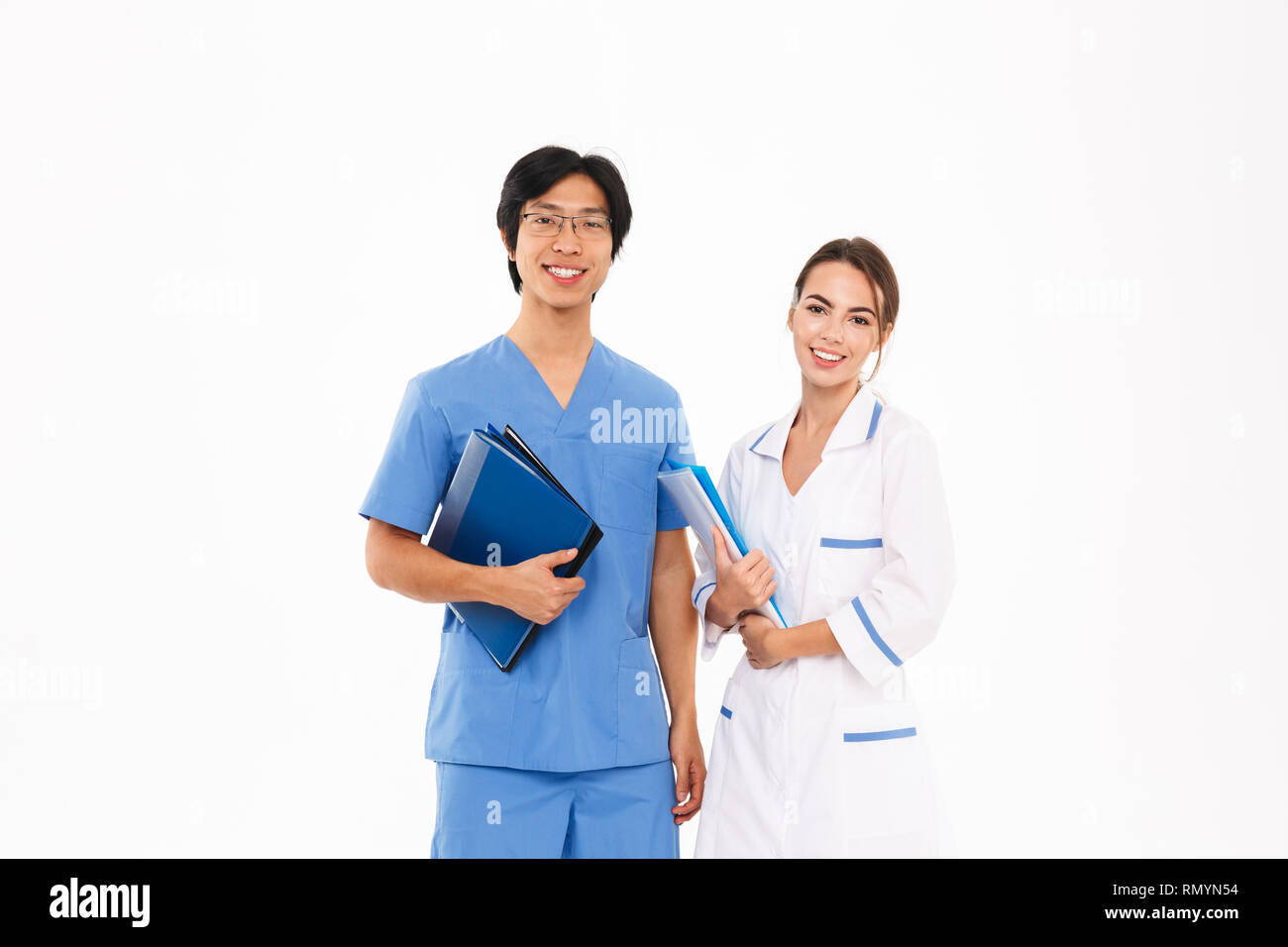 Smiling doctors couple wearing uniform standing isolated over white background, holding folders Stock Photo