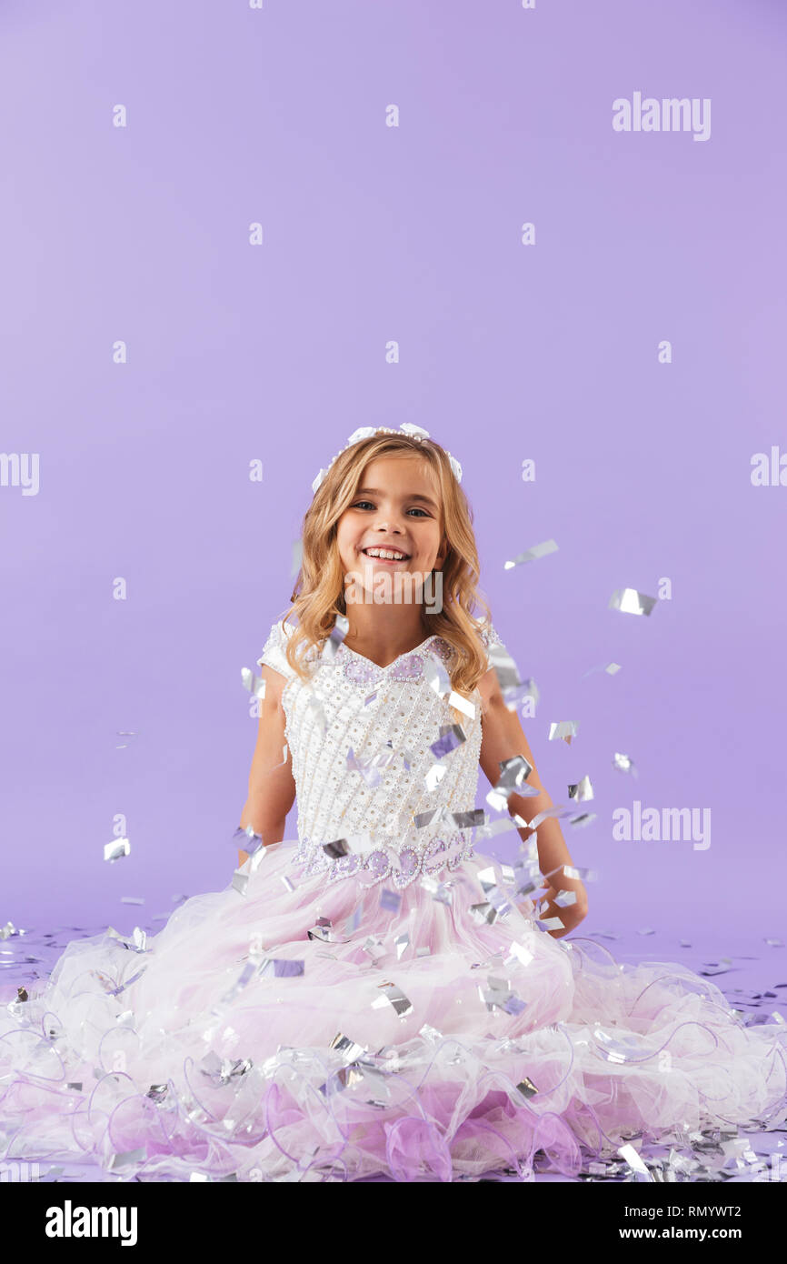 Pretty little girl dressed in princess dress sitting isolated over violet background Stock Photo
