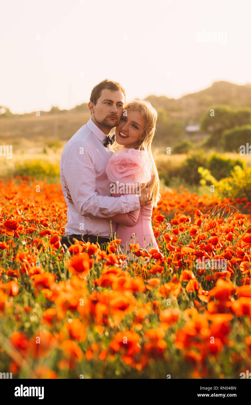 Man and woman embracing in poppy field on the dusk,  countryside Malta Stock Photo