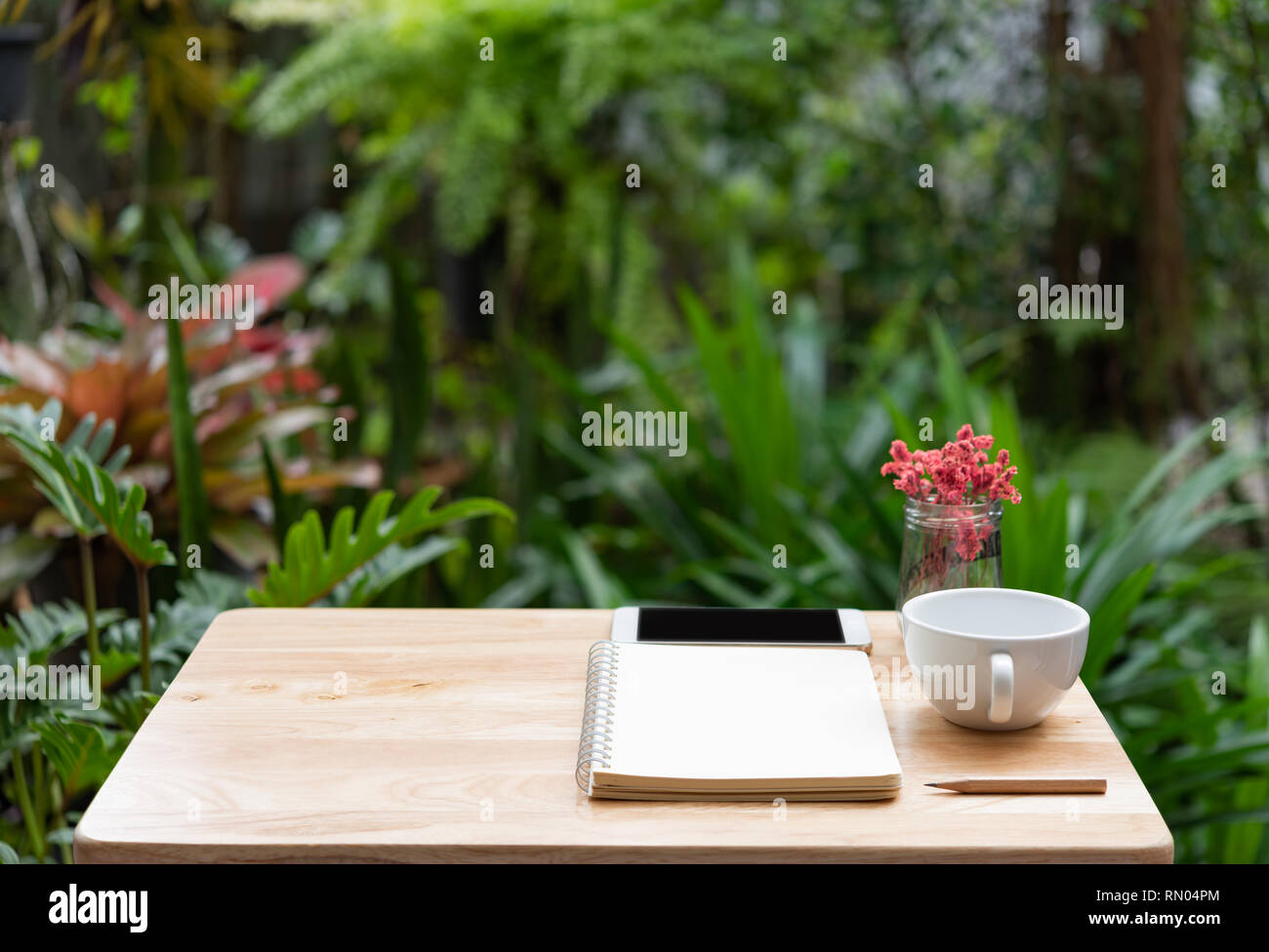Workspace outdoors with memo notebook,pencil,white coffee cup,mobile phone andd beautiful vase green nature background Stock Photo