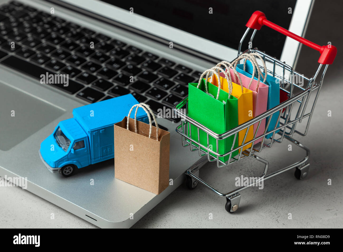 Delivery of orders from the online store. Shopping bags in shopping cart on  laptop keyboard and courier delivery truck Stock Photo - Alamy