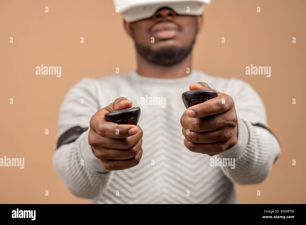 Dark-skinned millennial tourist in casual clothing wearing glasses with head-mounted display for smart phone, operating with controllers in hands, doi Stock Photo