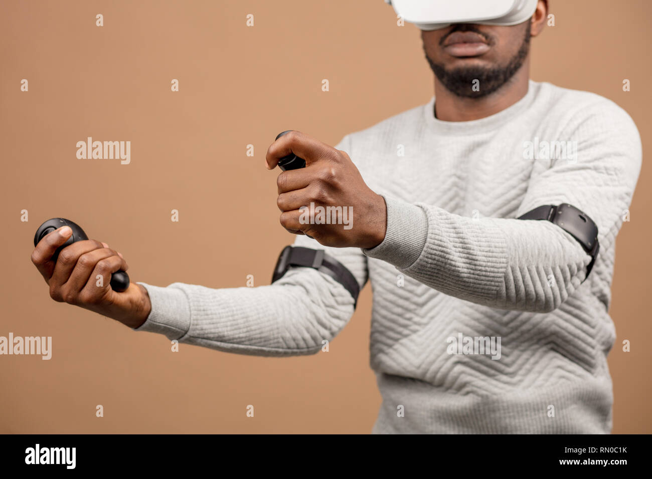 Dark-skinned millennial tourist in casual clothing wearing glasses with head-mounted display for smart phone, operating with controllers in hands, doi Stock Photo
