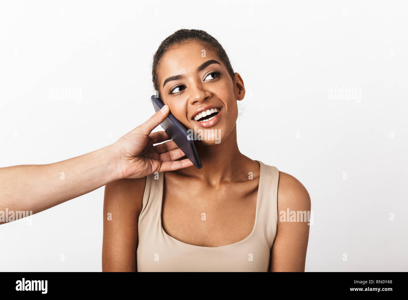 Happy young african woman sitting while man's hand holding mobile phone at her ear isolated over white background Stock Photo