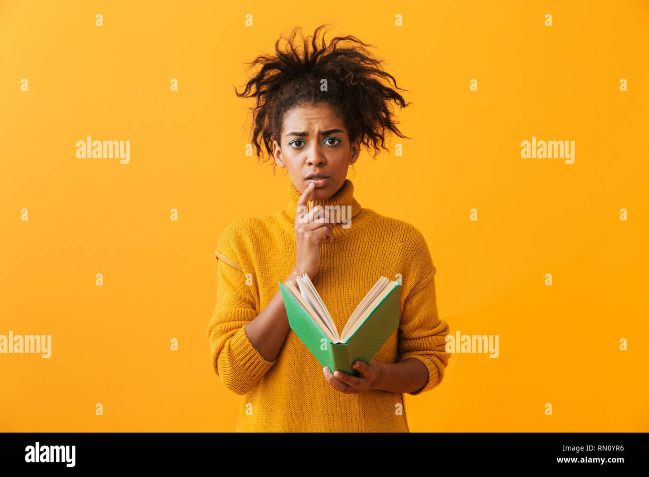 Confused african woman wearing sweater holding a book isolated over yellow background Stock Photo