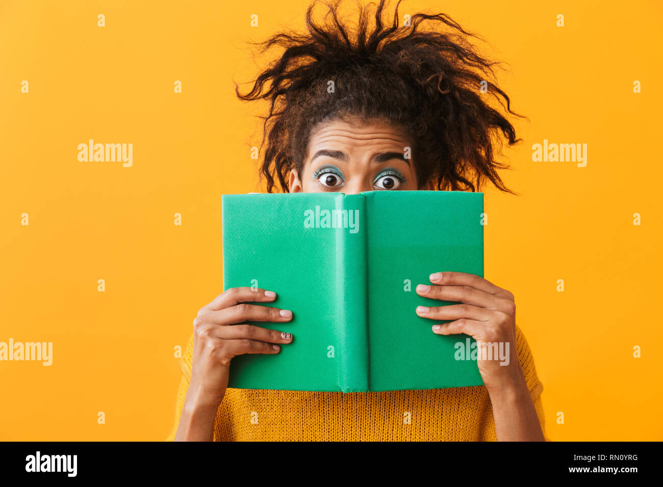 Confused african woman wearing sweater holding a book isolated over yellow background Stock Photo
