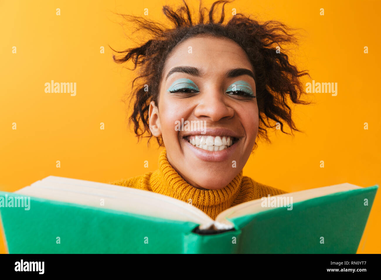 Cheerful african woman wearing sweater holding a book isolated over yellow background Stock Photo