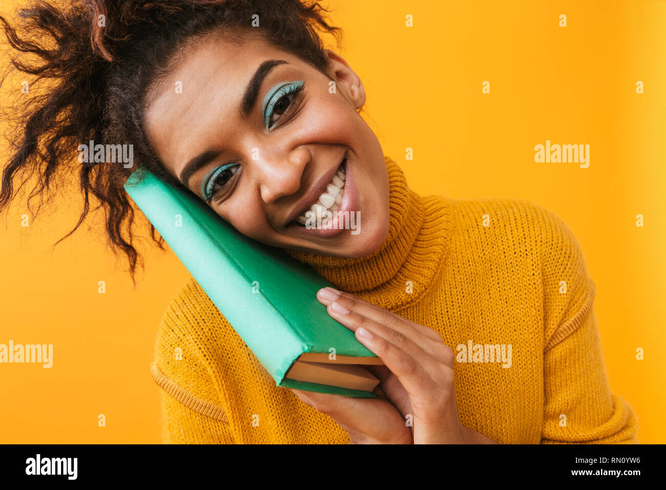 Cheerful african woman wearing sweater holding a book isolated over yellow background Stock Photo