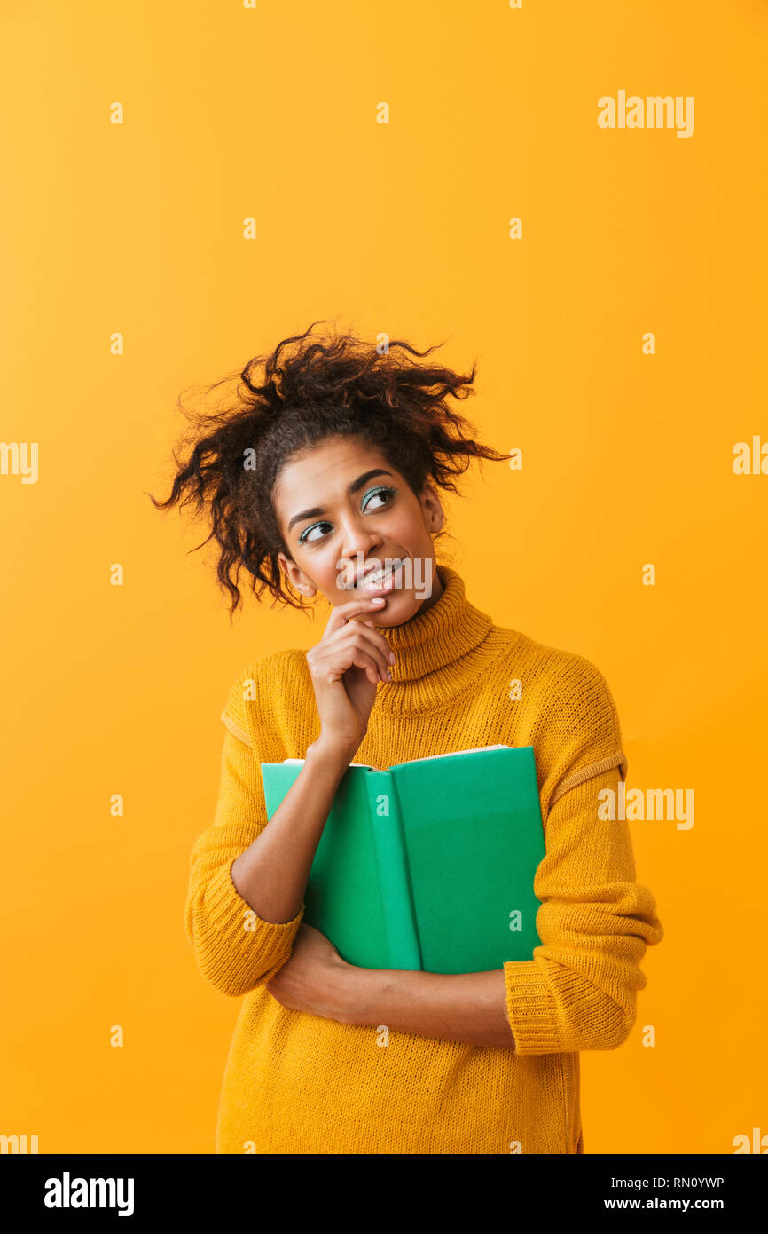 Cheerful african woman wearing sweater holding a book isolated over yellow background Stock Photo