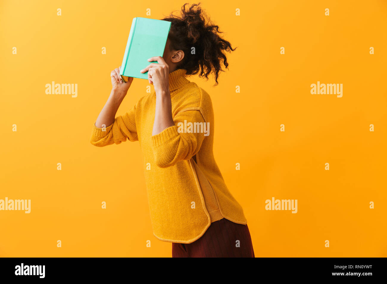 Funny african woman wearing sweater holding a book at her face isolated over yellow background Stock Photo