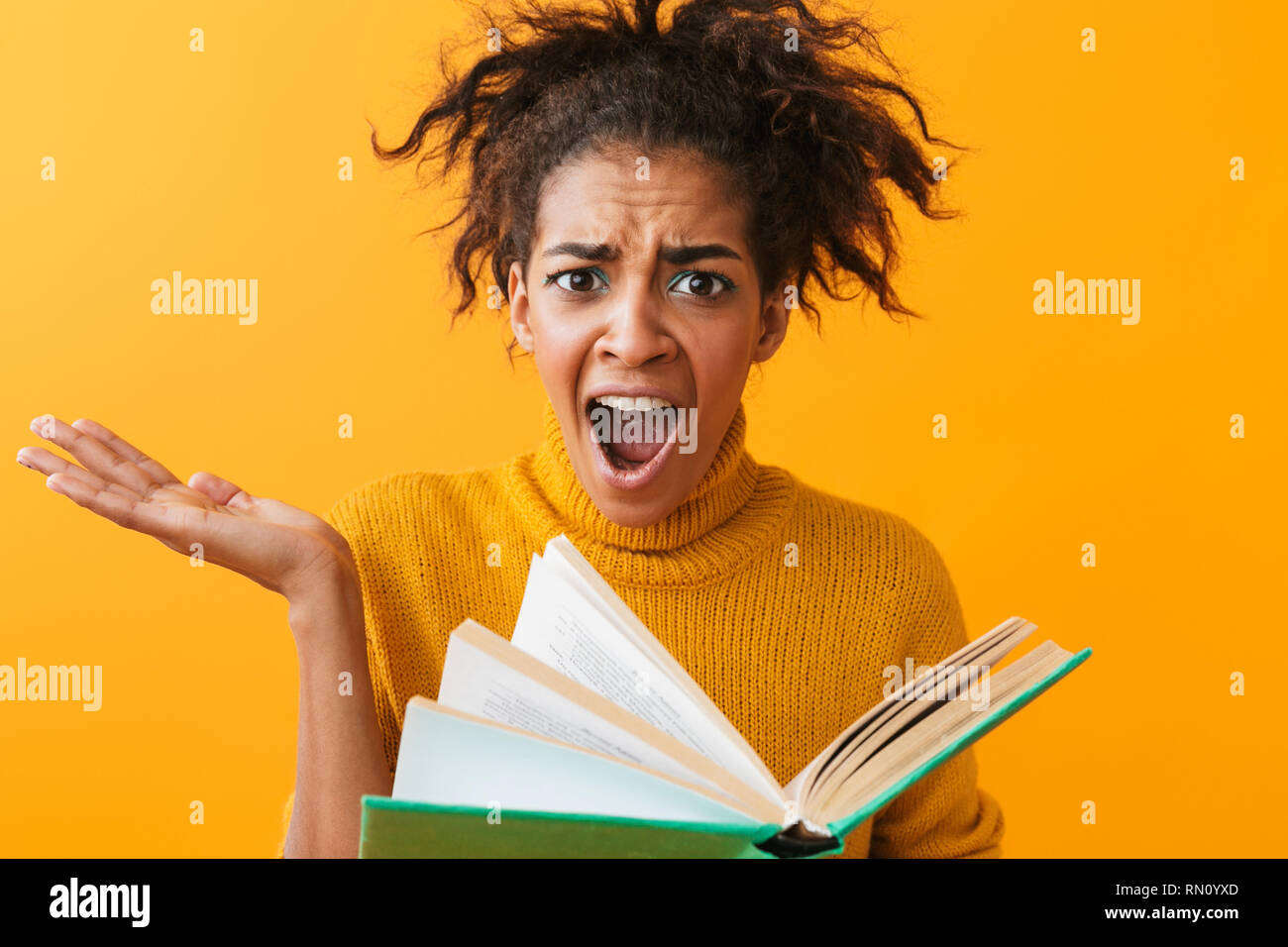 Cheerful african woman wearing sweater holding a book isolated over yellow background Stock Photo