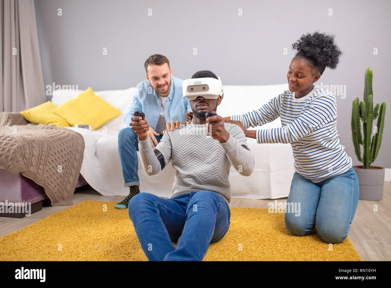 African male client testing 3D virtual reality headset playing video game while two diverse sales persons help him to take a purchase decision in shop Stock Photo
