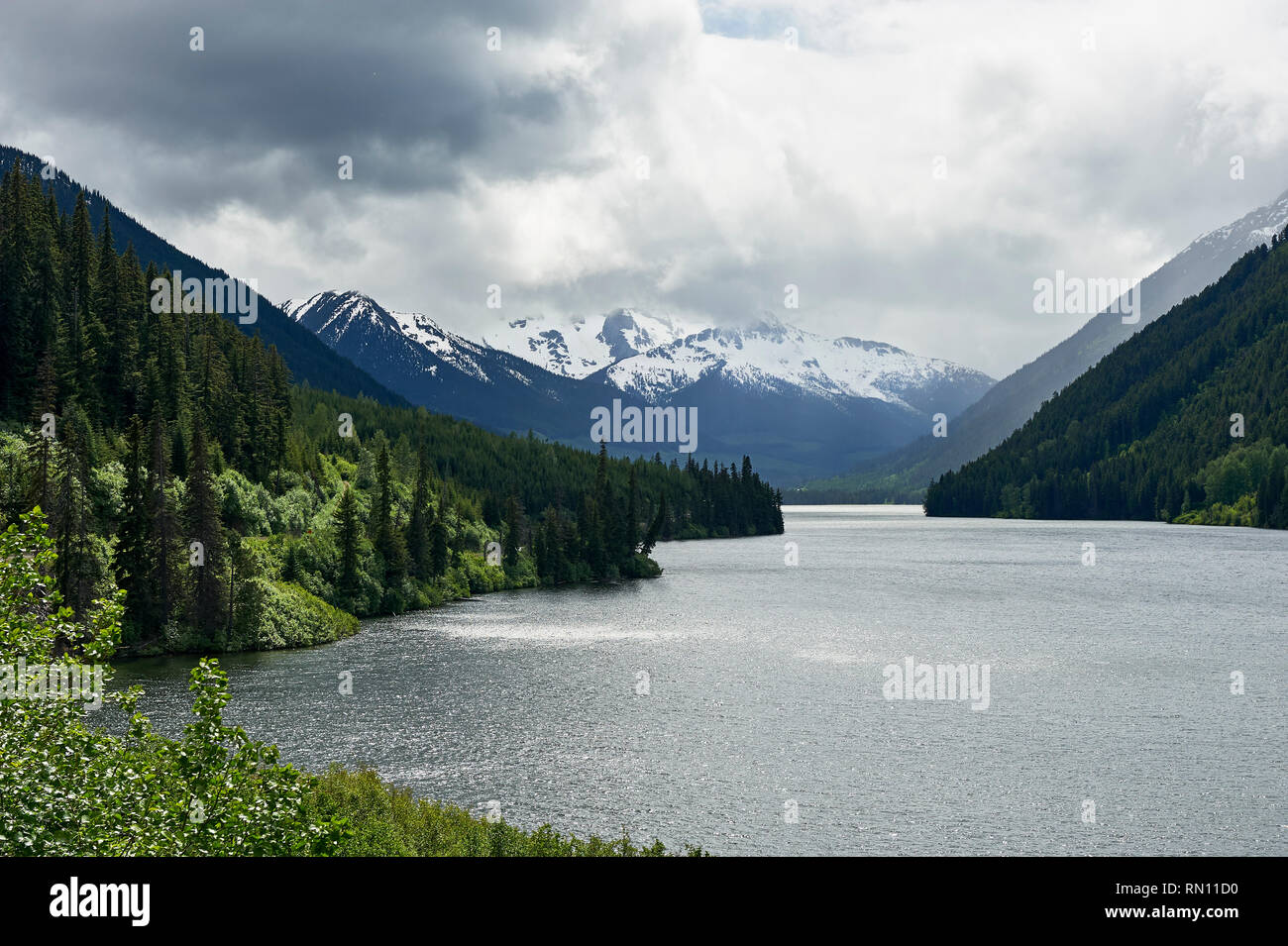 View at Duffey Lake, with overcast sky above snow covered mountains, surrounded by forest, along Highway 99, near Whistler, British Columbia, Canada Stock Photo