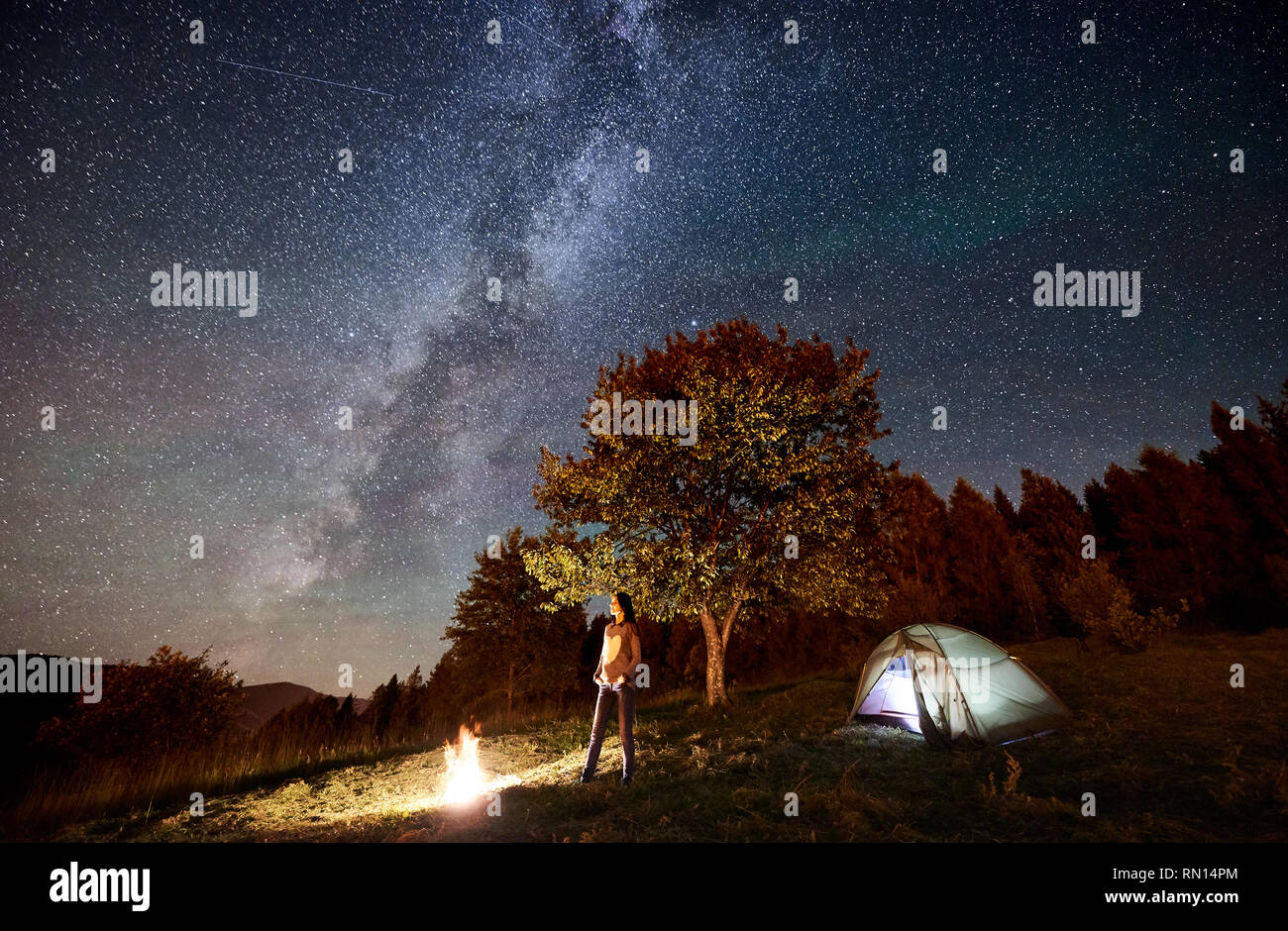 Happy Woman Traveller Having A Rest At Campfire Beside Camping And Glowing Tourist Tent Under Night Sky Full Of Stars And Milky Way On Background Beautiful Starry Sky Mountains And Big Tree Happy Woman Traveller Having A Rest At Campfire Beside Camping And Glowing Tourist Tent Under Night Sky Full Of Stars And Milky Way On Background Beautiful Starry Sky Mountains And Big Tree
