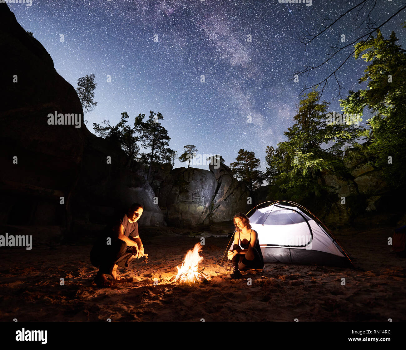 Young couple travellers man and woman resting beside camp, campfire and ...