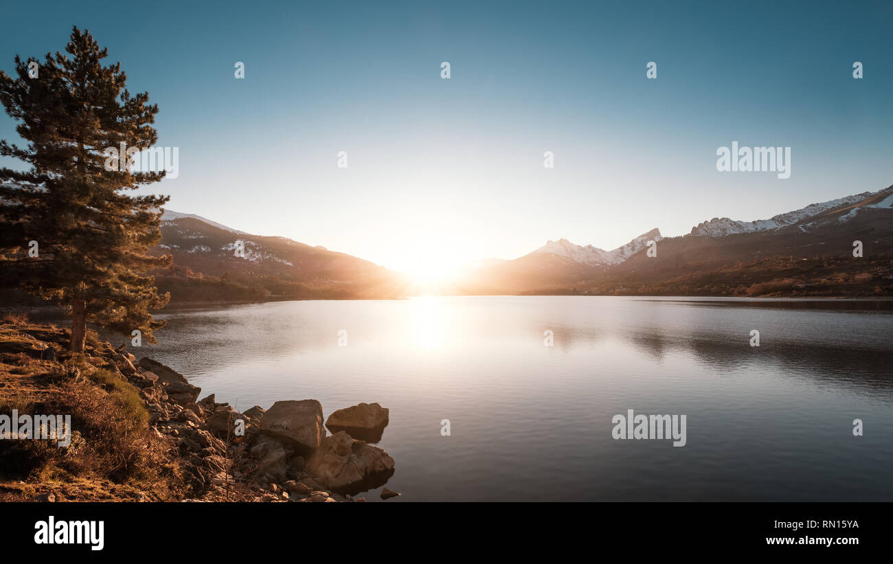 Sun setting behind snow capped mountains at Lake Calacuccia in central Corsica Stock Photo