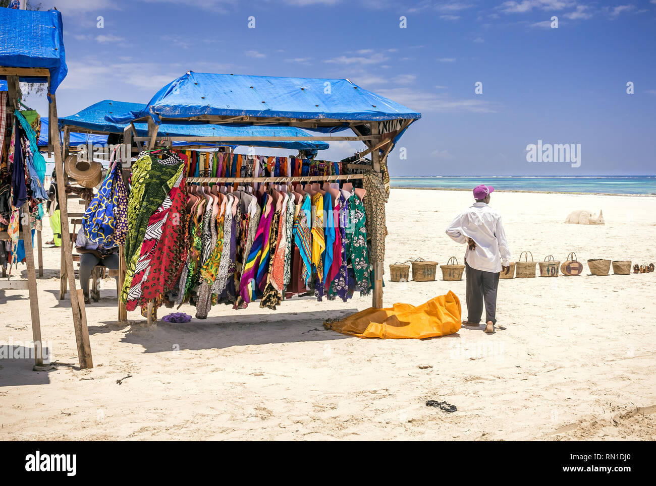 DIANI BEACH, KENYA - OCTOBER 10, 2018: Native african man and typical wooden stall with colorful fabrics on Diani beach, Kenya Stock Photo