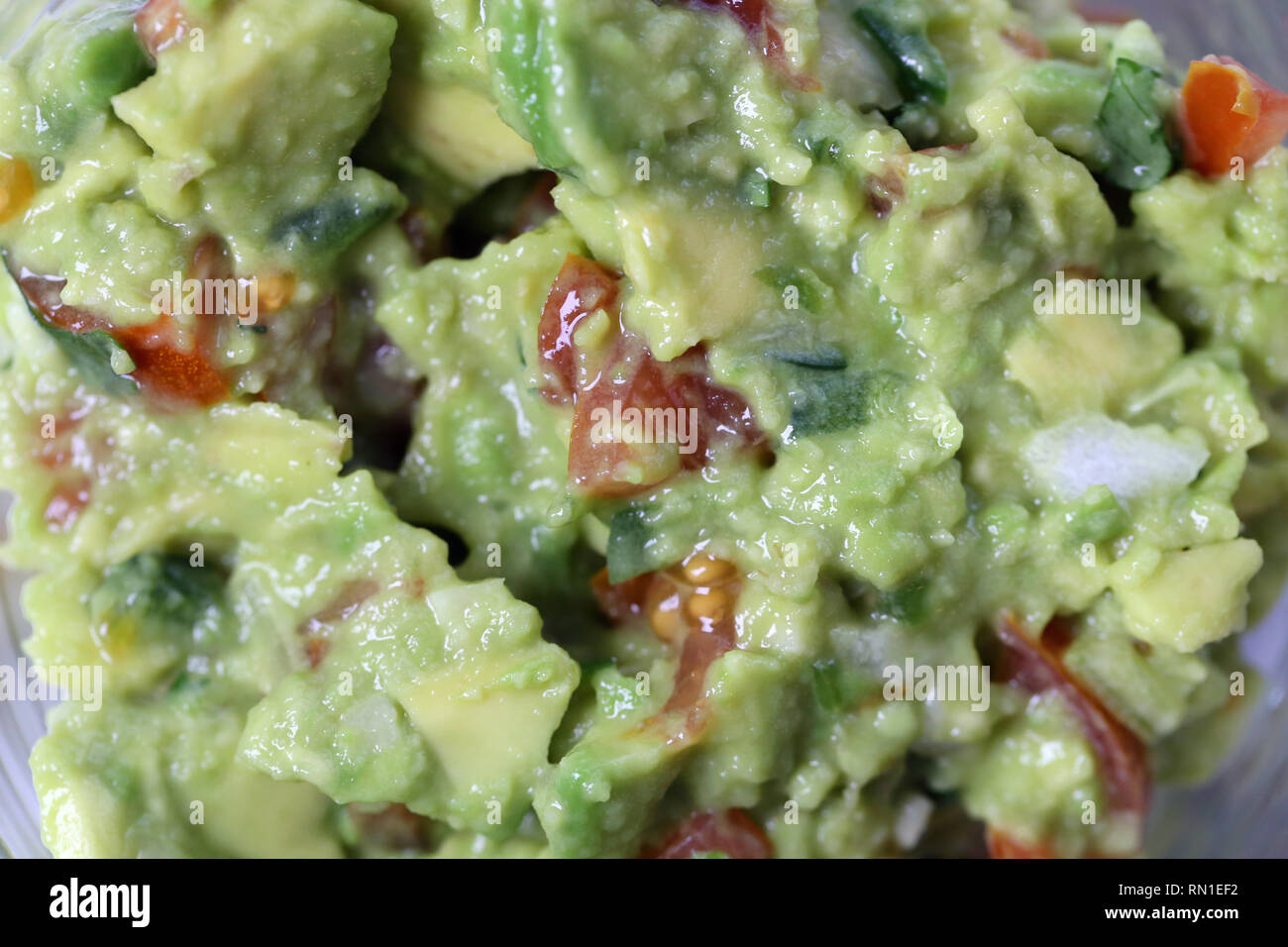 Macro photo of the texture of slightly chunky guacamole, a Mexican dip often eaten with crunchy nachos. Healthy and delicious food. Stock Photo