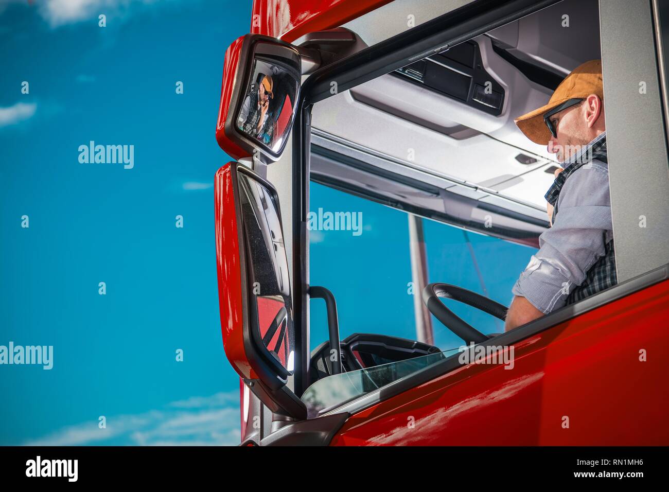 Transportation Industry Theme. Caucasian Truck Driver in His 30s Inside the Red Semi Cabin. Stock Photo