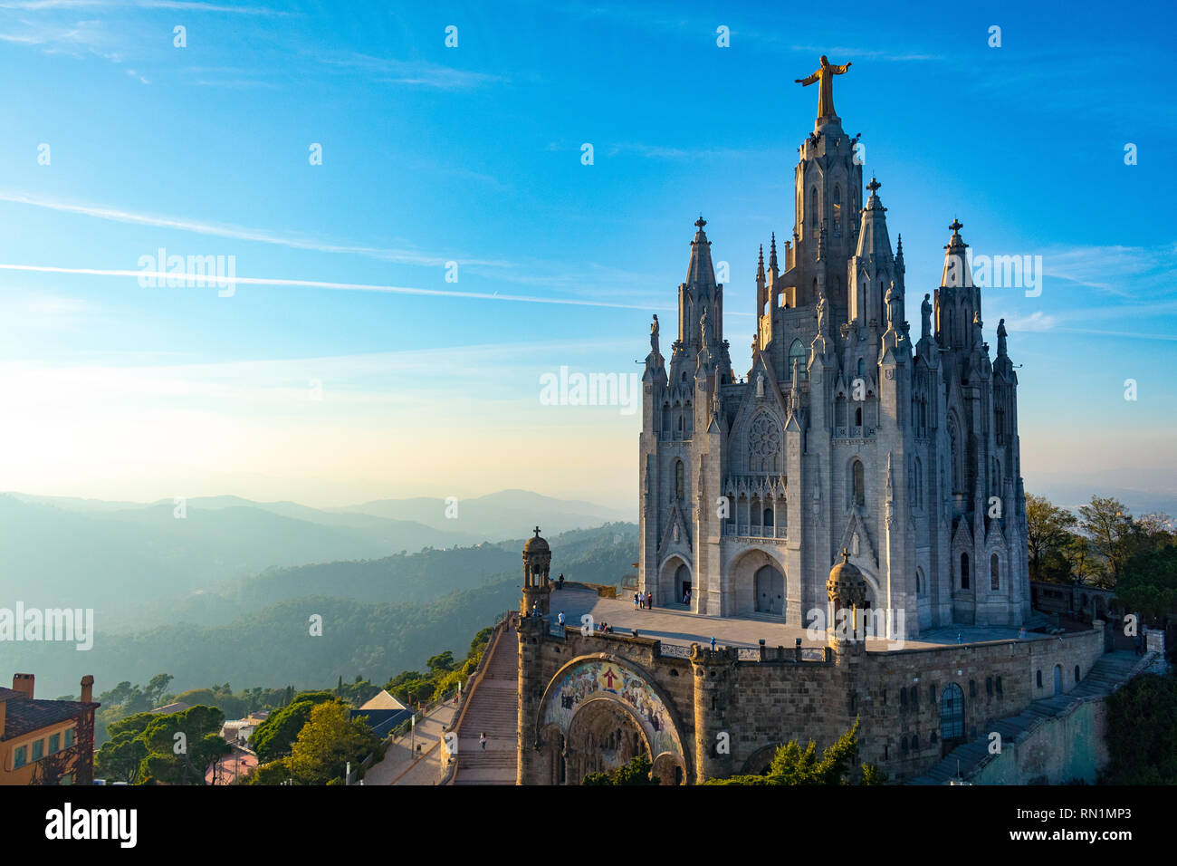 View of Tibidabo Cathedral, Barcelona. Captured at sunset with the warm glow across the tree covered hills in the background. Taken at a raised view - Stock Image
