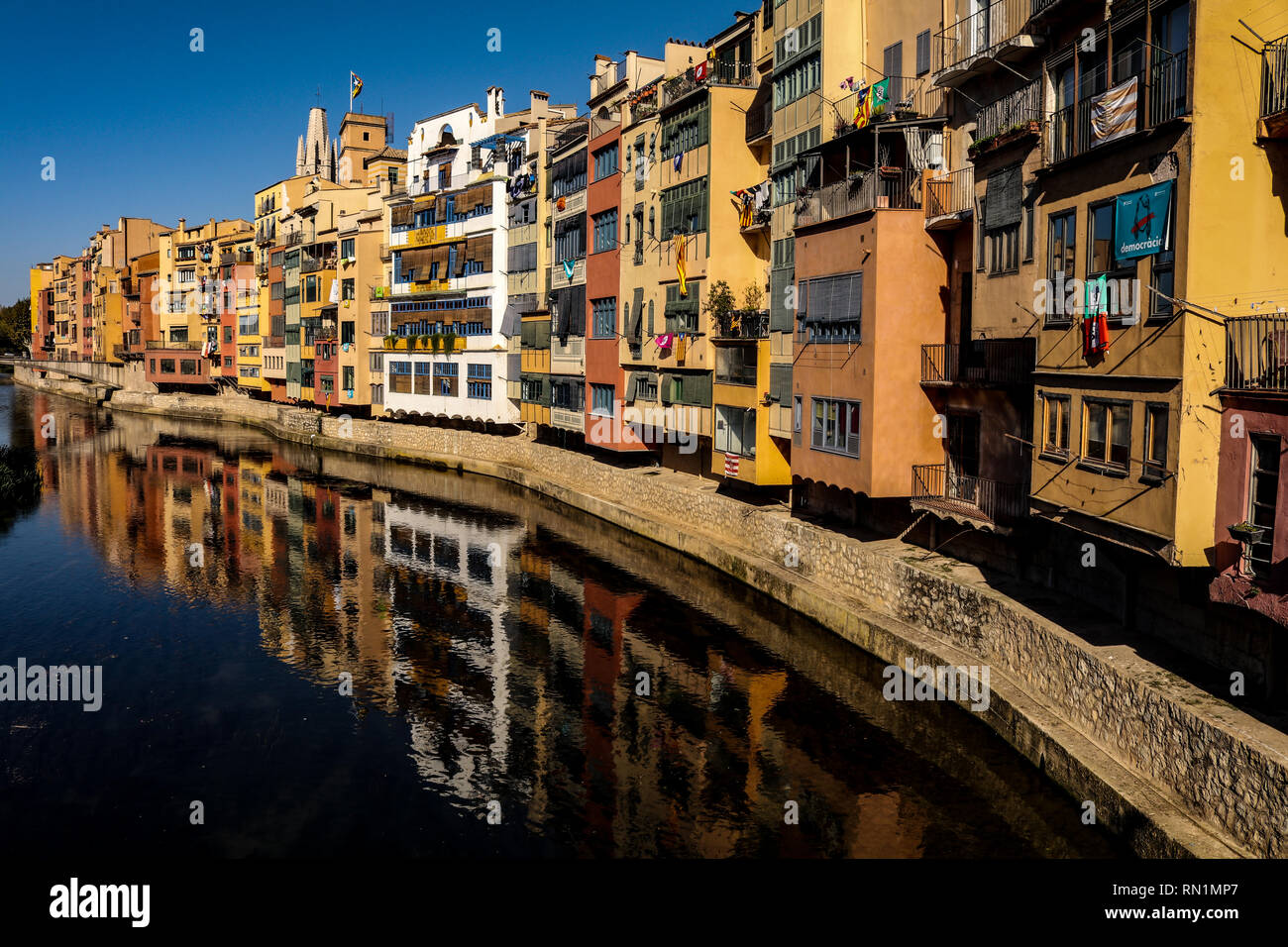 View of colourful buildings overlooking the river in Girona, with a reflection back onto the waterfront, saturated and deep colours. - Stock Image