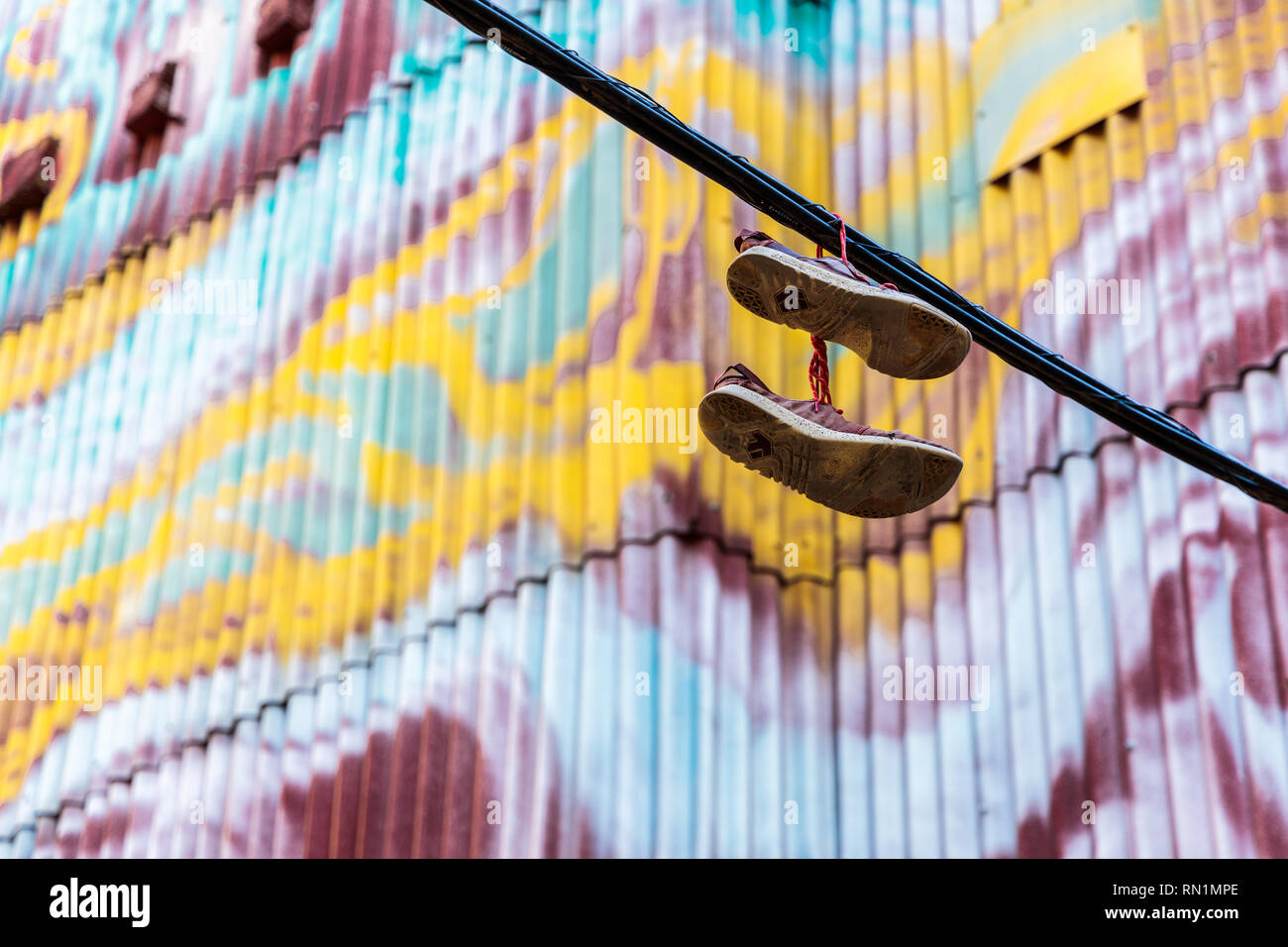 Pair of shoes hanging from a cable with a graffiti background - Stock Image
