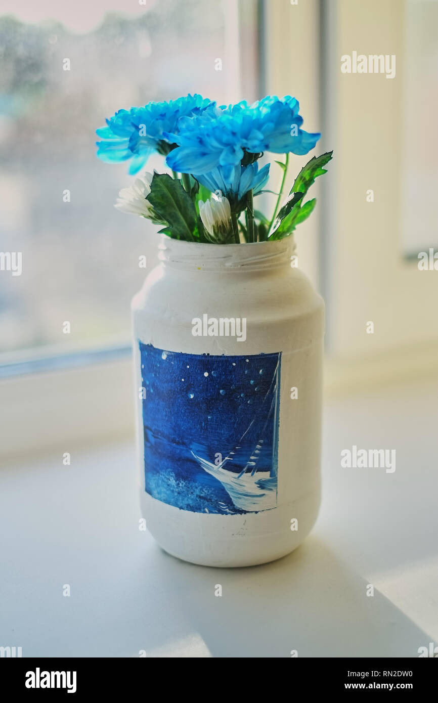 Cornflower flowers in a white jug. The jug stands on a white window sill. bouquet of flowers in a jar painted with paints. Stock Photo