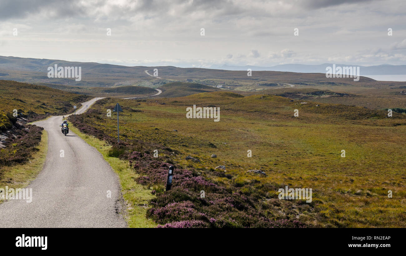A motorcyclist and passenger ride across moorland at Cuaig near Applecross on the North Coast 500 route in the remote Highlands of Scotland. Stock Photo