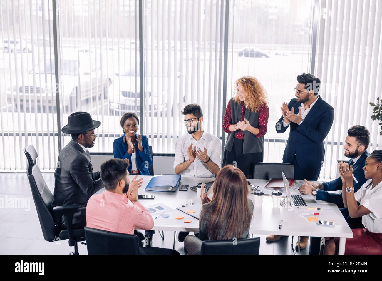 Red-haired woman boss and her Indian male assistant applaud to african man wearing hat on head, who gives a amazing business strategy idea during meet Stock Photo