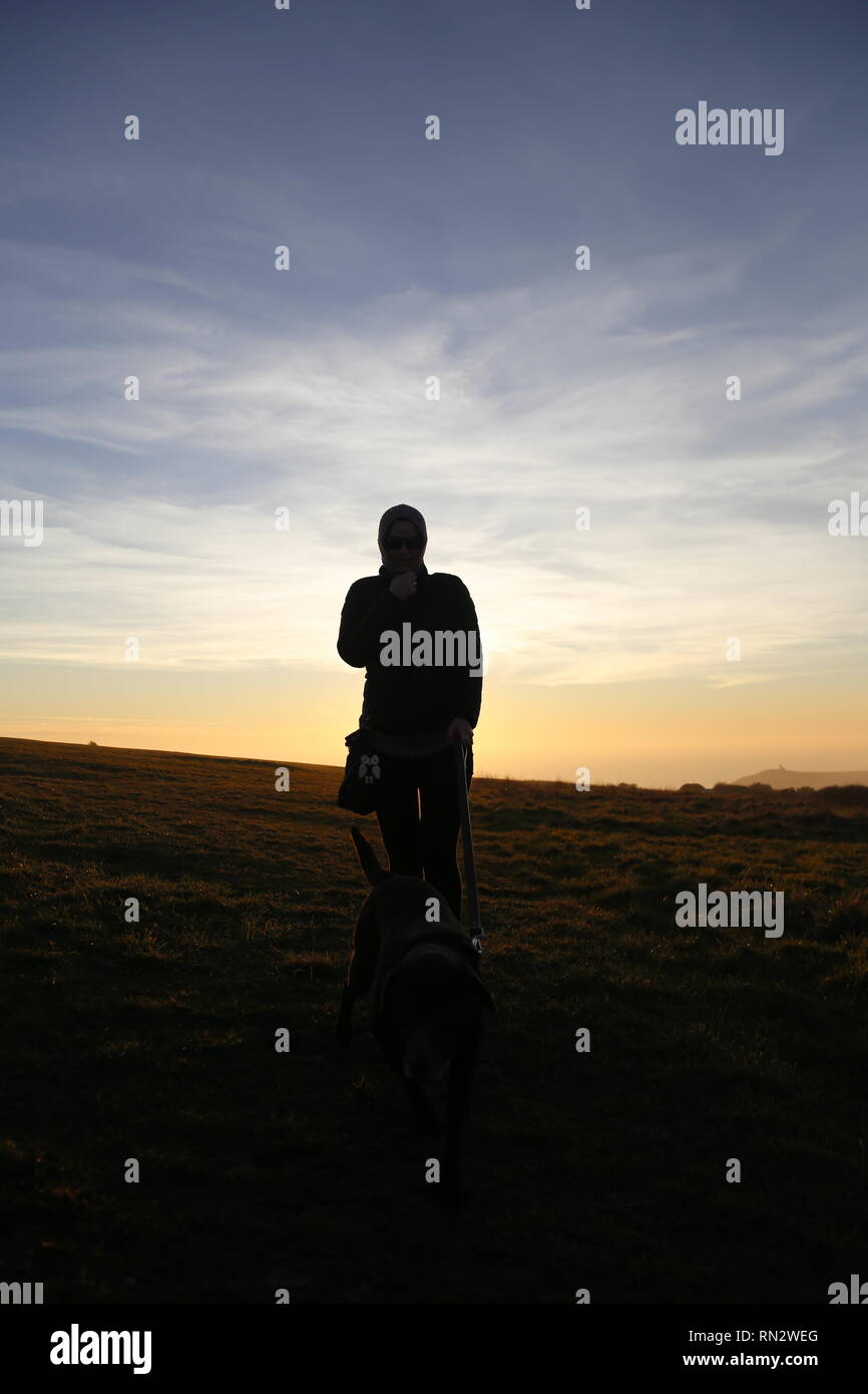 Woman with dog walking toward camera at sunset Stock Photo