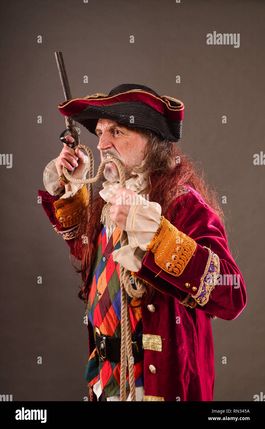 Sea dog, old pirate with musket, holding rope by teeth, studio shot against gray background Stock Photo