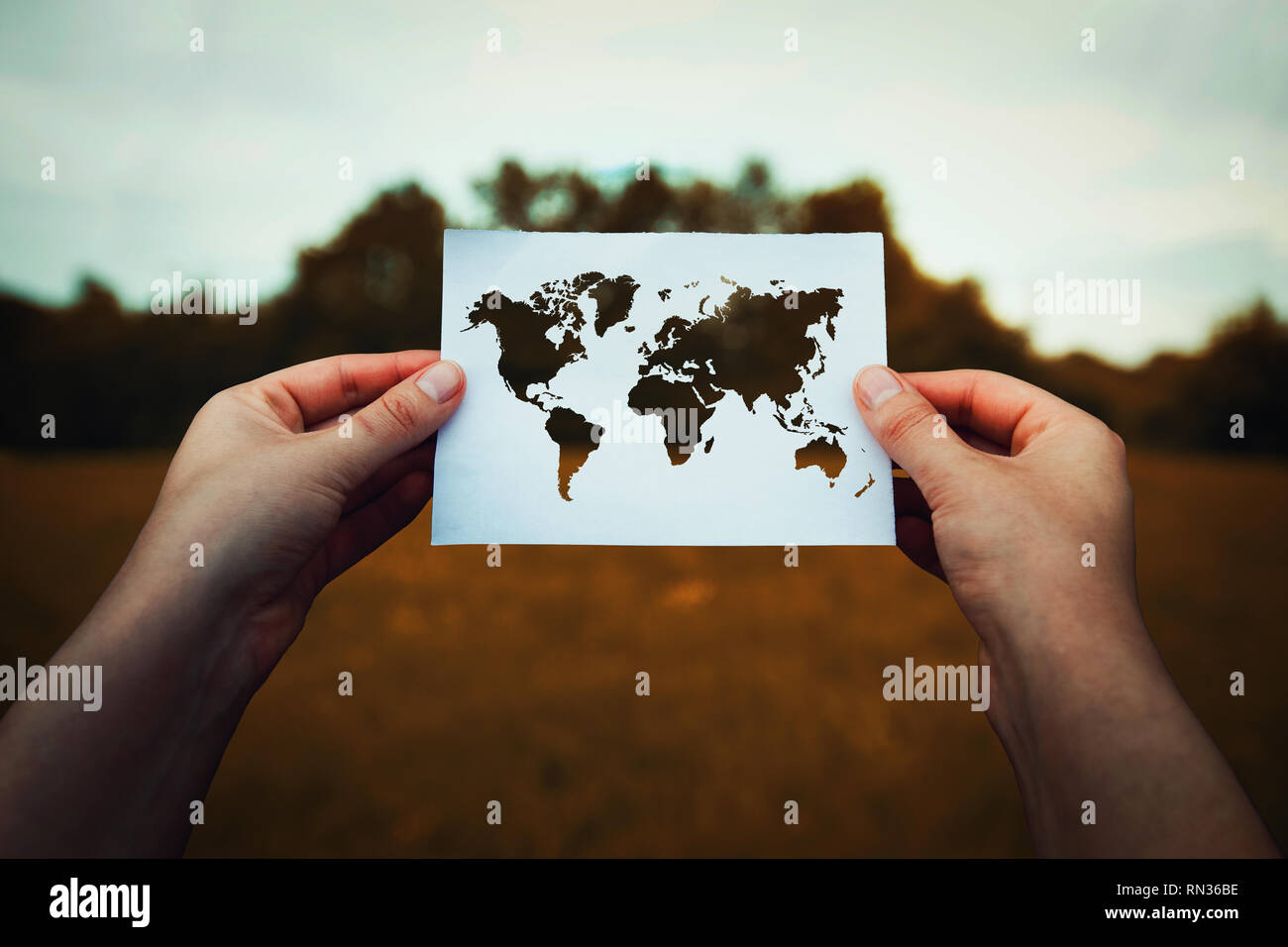Climate change problem, destruction of nature concept. Human hands holding a paper sheet with world map icon over a dry grass field background. Global Stock Photo