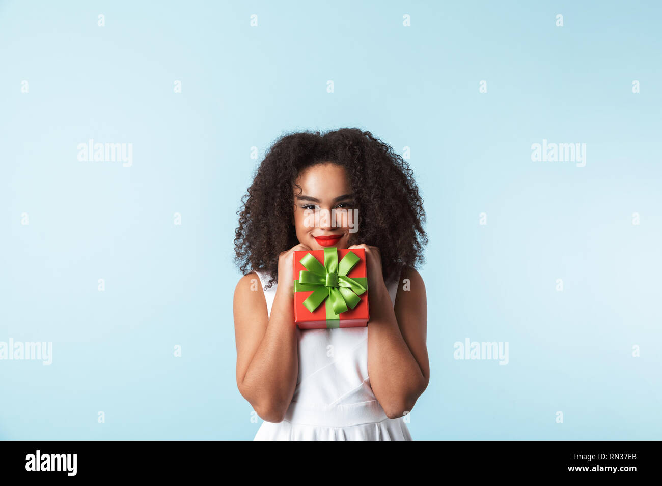 Cheerful young african woman wearing dress celebrating isolated, holding present box Stock Photo