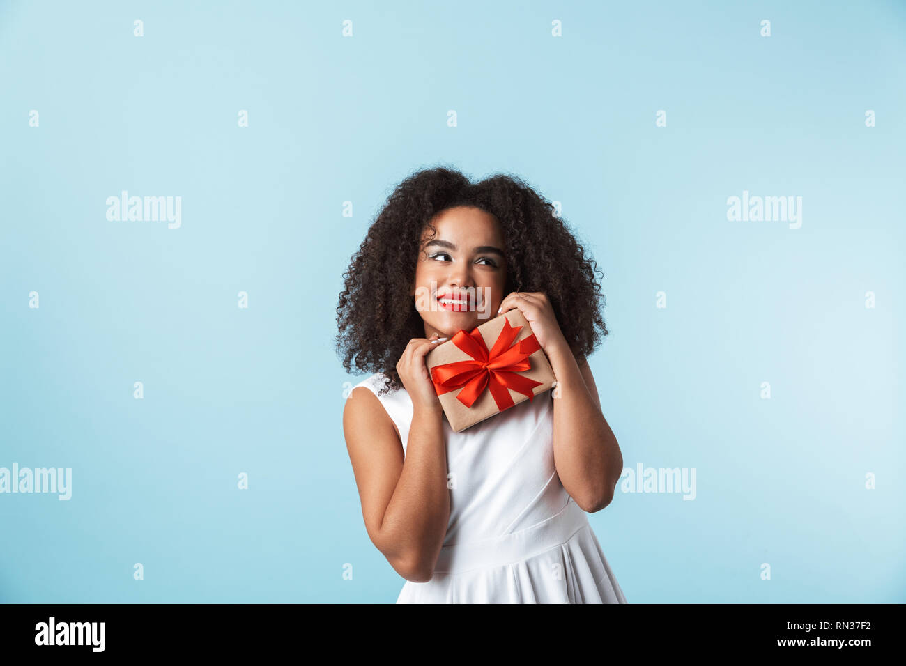 Cheerful young african woman wearing dress celebrating isolated, holding present box Stock Photo