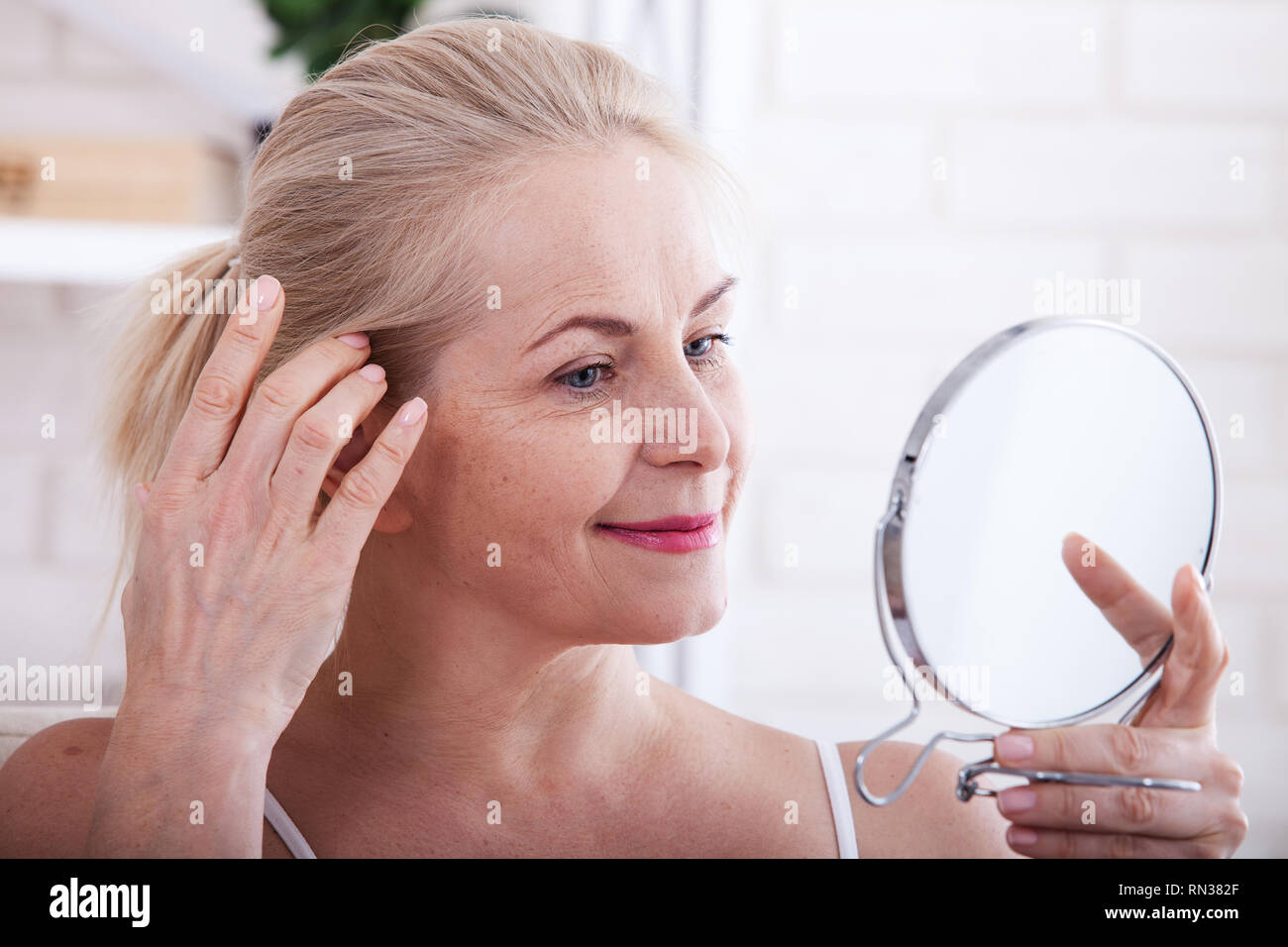 Middle aged woman looking at wrinkles in mirror. Plastic surgery and collagen injections. Makeup. Macro face. Selective focus on the face. Realistic images with their own imperfections. Stock Photo