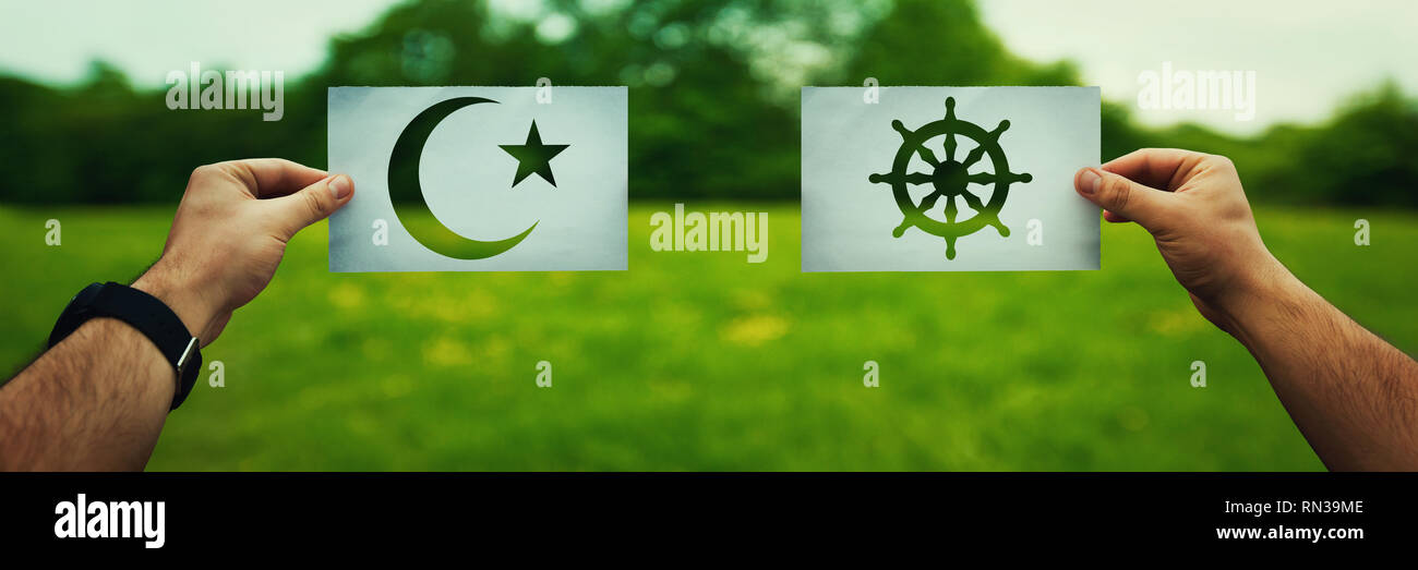 Religion conflicts as global issue concept. Two hands holding different faith symbols, Islam vs Buddhism belief over green field nature. Relationship  Stock Photo