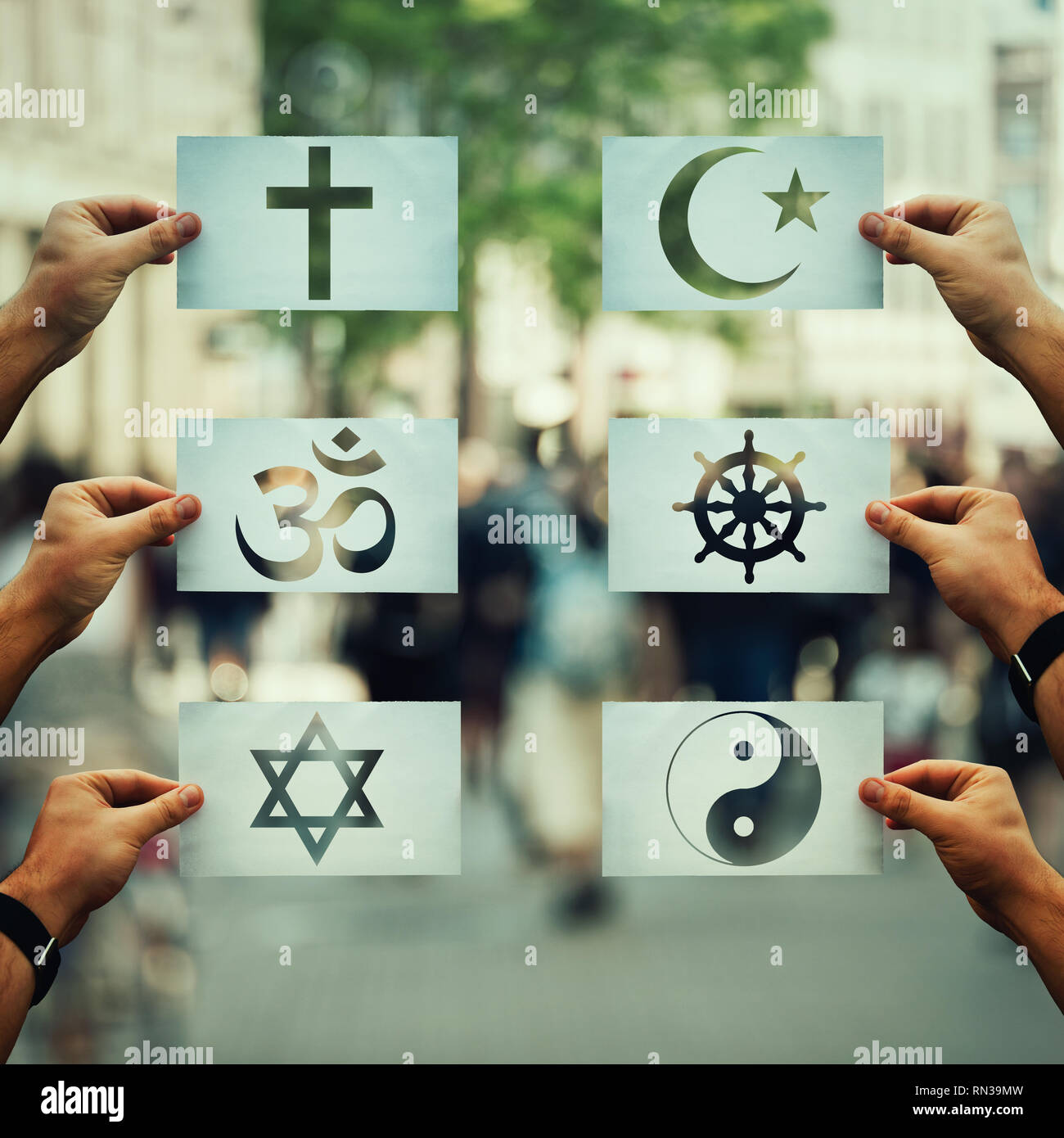 Religion conflicts as global issue concept. Human hands holding different paper with faith symbols over crowded street scene. Relations between differ Stock Photo