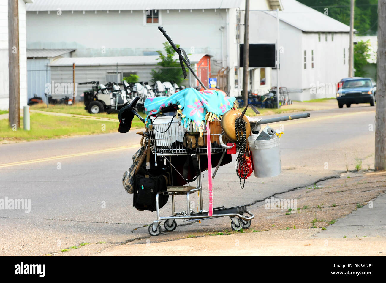 Homeless man's possessions fill this lone shopping cart parked on the side of a city street.  A blanket covers his belongings that spill over the side Stock Photo
