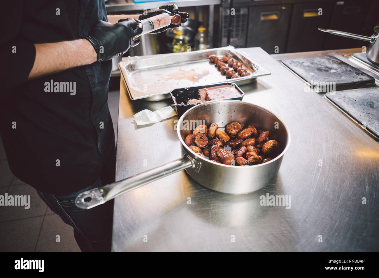 Theme cooking. Hands close up. young Caucasian man in black uniform and latex gloves in kitchen. restaurant prepares ground beef and leads into berry  Stock Photo