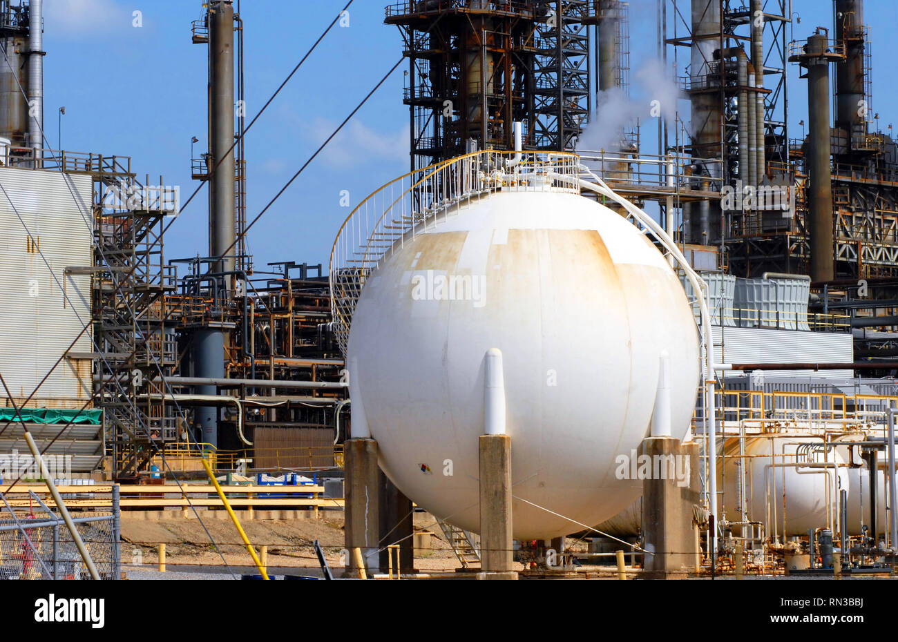 Large white storage tank at oil refinery has spiral stairs winding