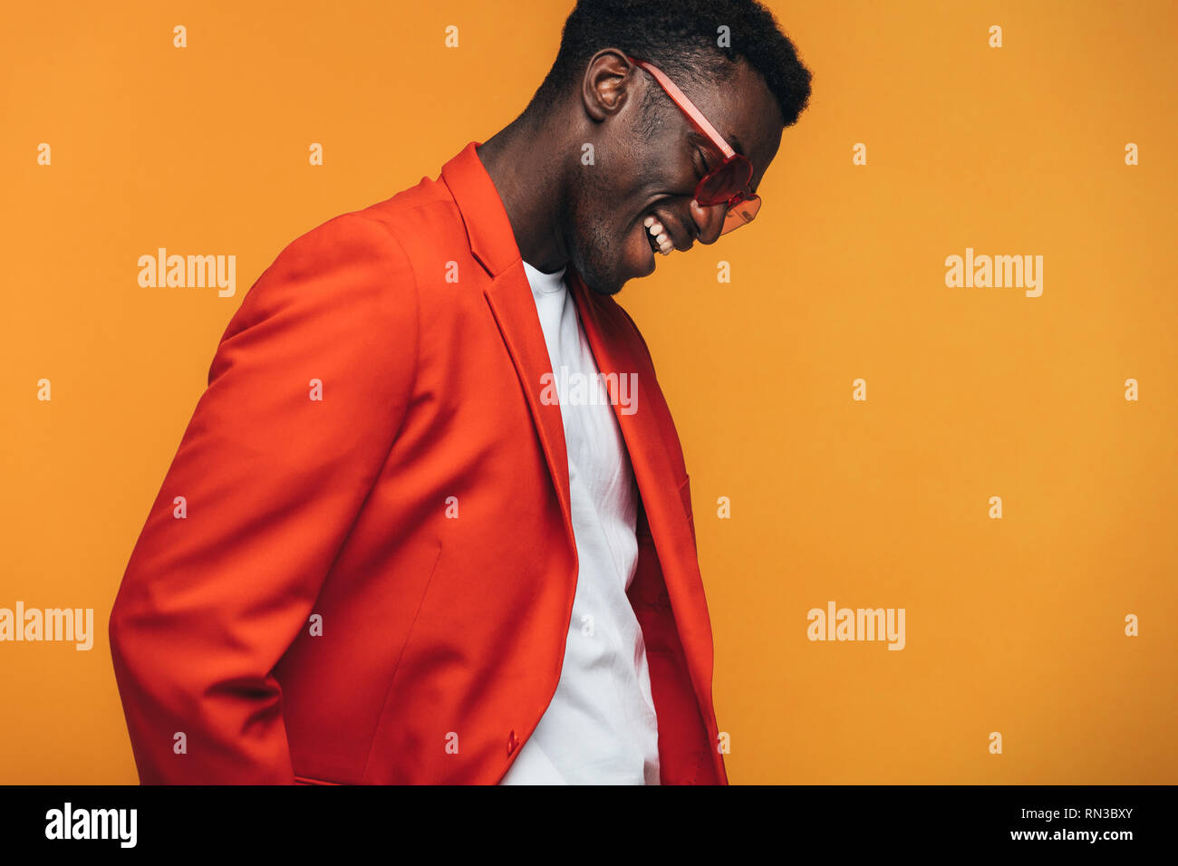 Handsome african male fashion model with sunglasses smiling against orange background. Stylish african man smiling in studio. Stock Photo