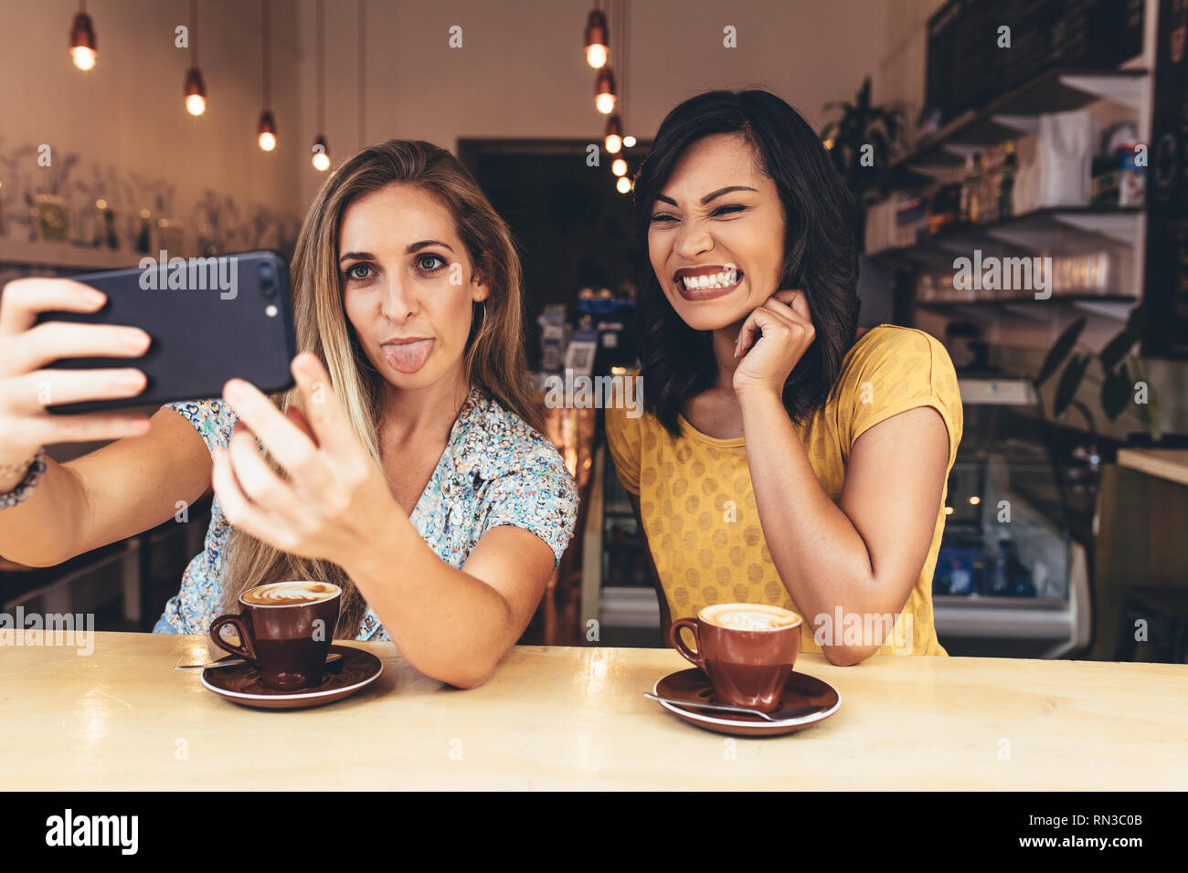 Woman sticking out her tongue while taking selfie with a smiling friend