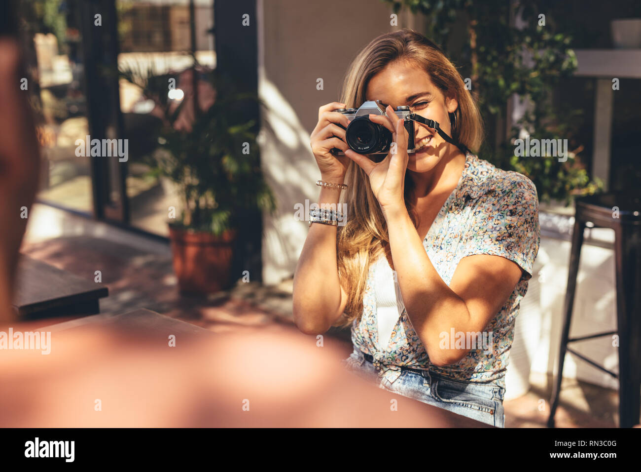 Woman taking pictures of her friends with digital camera while sitting at cafe. Man getting his photos clicked by a female friend for this social medi Stock Photo
