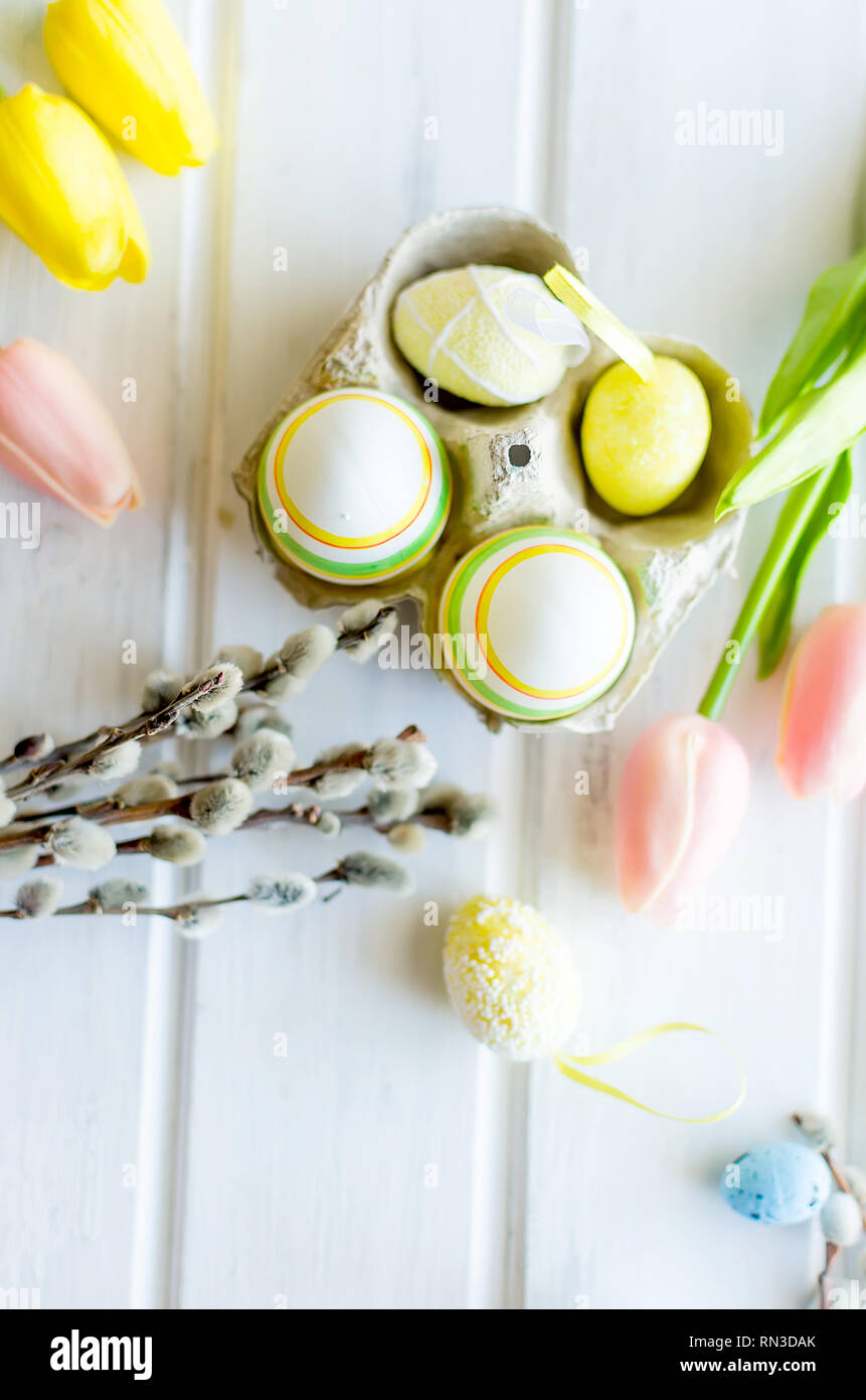 yellow tulips, ginger cookies, willow twigs, decorative eggs in a tray laid out on a white old wooden table, easter holiday background with sweets, fl Stock Photo