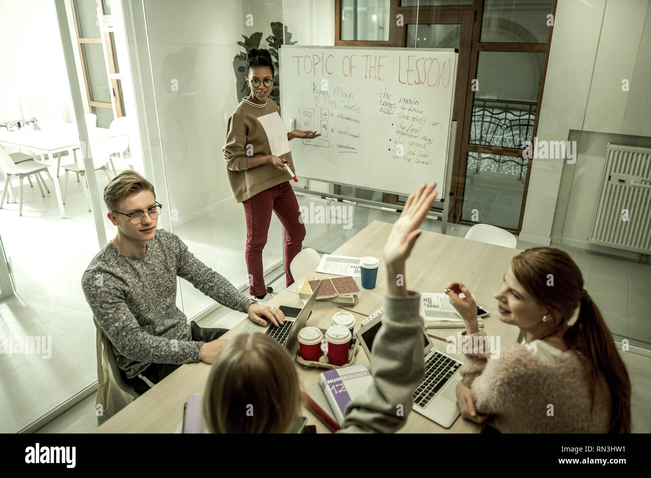 Student wearing grey sweatshirt raising hand asking question Stock Photo