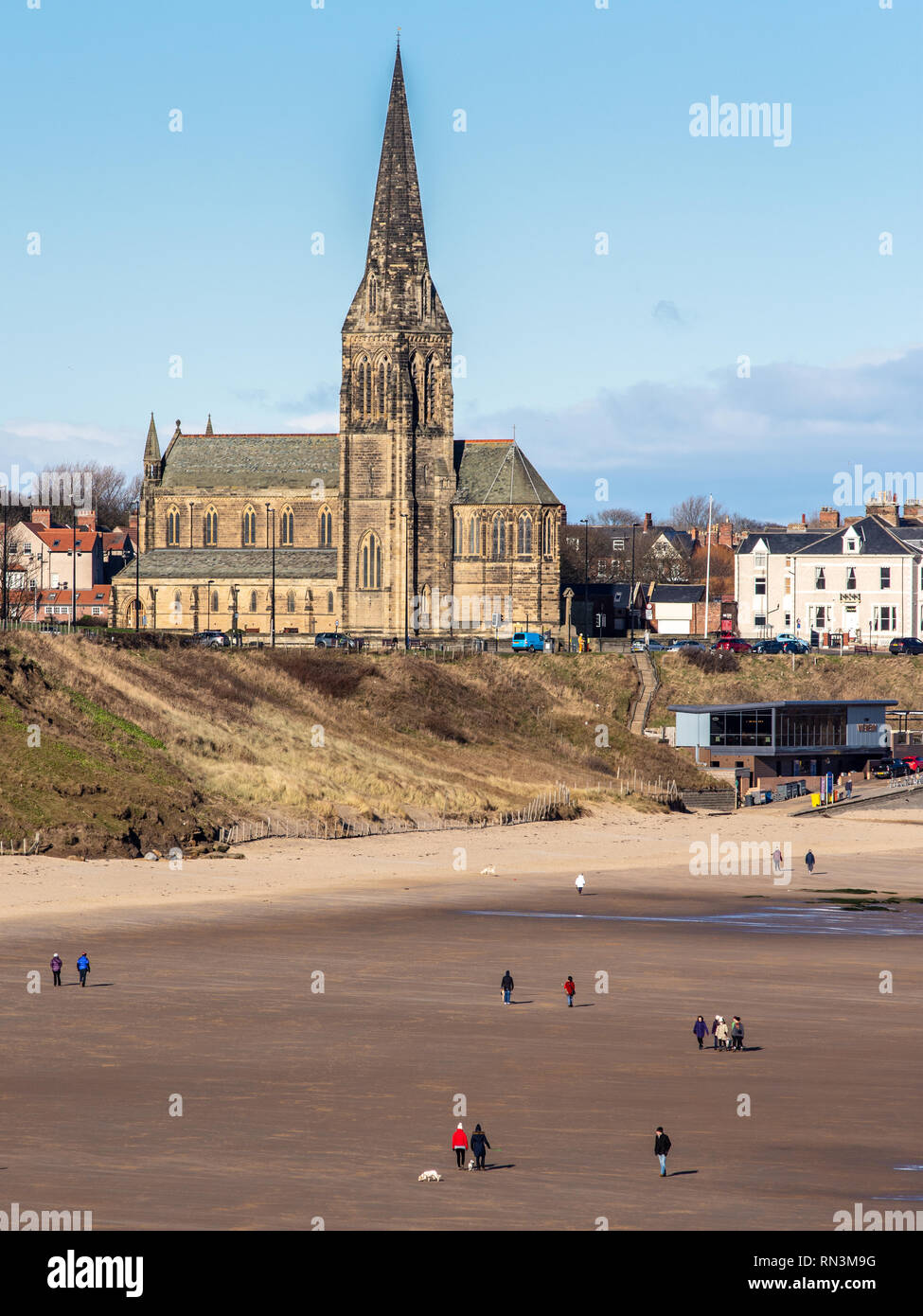 Tynemouth, England, UK - February 4, 2019: People walk their dogs on the expansive beach of Tynemouth Longsands on a sunny winter day, with Cullercoat Stock Photo